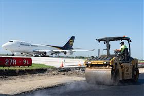 Haines & Kibblehouse, Inc.: A Caterpillar asphalt roller works on base as a UPS 747 prepares for takeoff. 