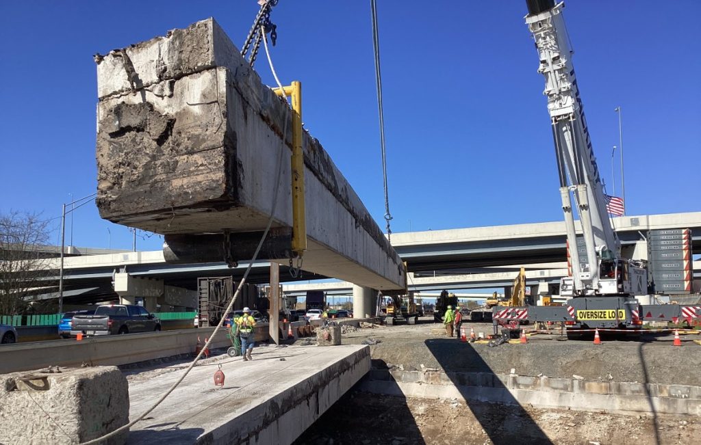 Crane removing a large concrete bridge beam in the I-95 interchange construction area