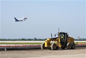 Haines & Kibblehouse, Inc.: As a Fedex cargo plane takes off, a Caterpillar 12M3 grades stone before paving begins.